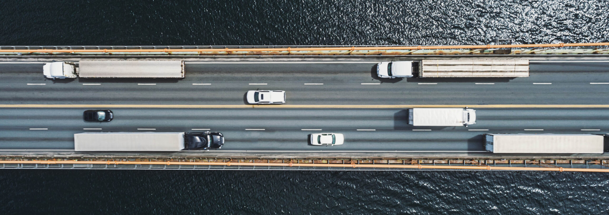 Overhead image of busy highway with trucks and cars on bridge over water.